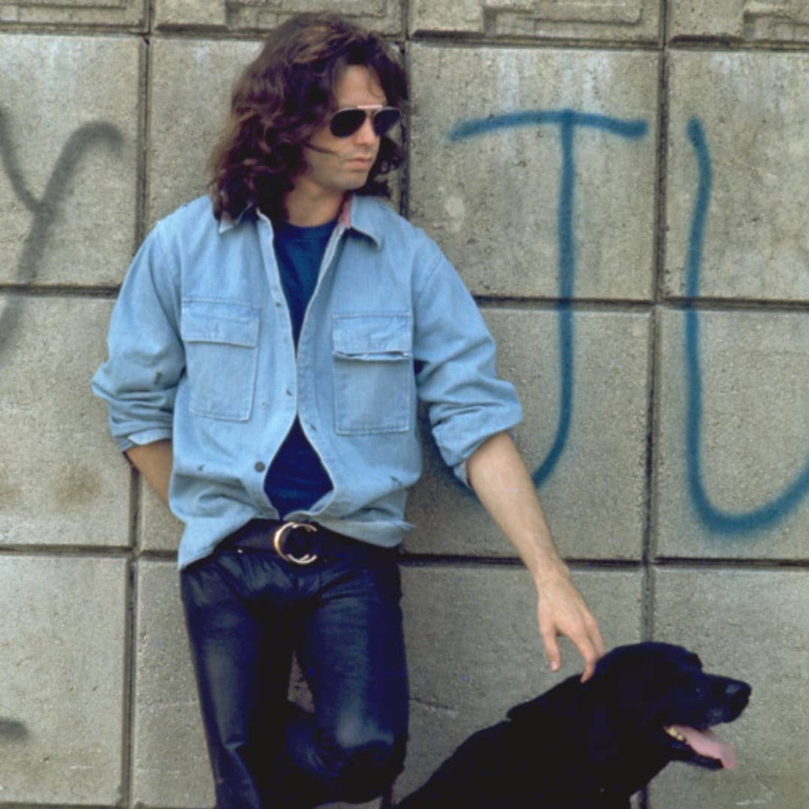 Jim Morrison posing with a black dog in the street, Photo Credit: Jim Morrison/Facebook